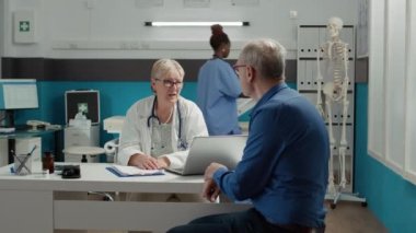 Genel pratisyen doktor, muayene randevusunda emekli bir hastayla konuşuyor. Doktor, yaşlı bir adama muayenehanede hastalık konusunda danışmanlık yapıyor. İyileşmesi için tedavi uyguluyor..