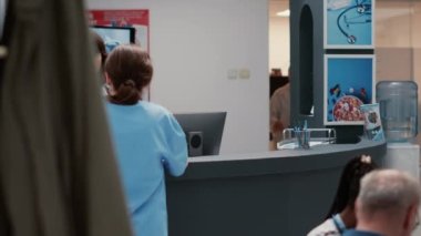 Medical staff and secretary talking at hospital reception desk, working on administrative information service in clinic lobby. Receptionist and medic chatting in waiting room area.