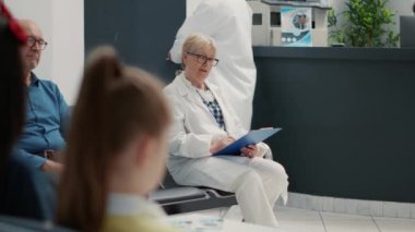Portrait of senior medical specialist sitting in waiting area lobby at healthcare facility, general practitioner taking notes before doing checkup visit and consultation. Hospital reception desk.