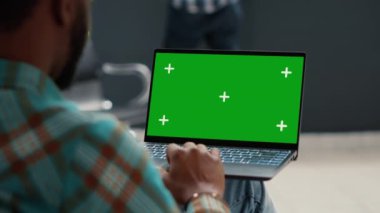 Male patient using greenscreen display on laptop computer, sitting in hospital reception lobby. Looking at isolated chroma key background with mockup template and blank copyspace. Close up.