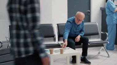 Bekleme alanında oturan kıdemli bir hastaya tıbbi danışmanlık asistanı teşhis hakkında notlar almak için dosya raporunu kullanıyor. Hasta bakıcı ve emekli adam hastane lobisinde muayene yapıyor..