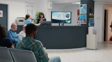 Busy hospital reception with diverse group of patients in waiting room area, having consultation appointment with specialist for healthcare treatment. Reception desk in facility lobby.
