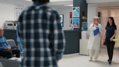 Busy hospital reception desk with diverse people in waiting room, asian and african american man using reports to attend medical appointment. Waiting room lobby at facility clinic.