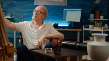 Beyaz tuval üzerine vazo tasarımı çizen fiziksel engelli kıdemli bir sanatçı, eskiz başyapıtı yaratıyor. Engelli erkek tekerlekli sandalye kullanıcısı sanat eserleri yaratmak için sanatsal beceriler kullanıyor.