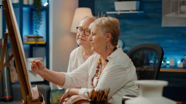 Kıdemli sanatçılardan oluşan bir ekip, ahşap sehpalı beyaz tuval üzerine resim çizmek için yaratıcı yetenekler kullanıyor. Kalemler ve sanatsal ekipmanlarla profesyonel şaheser çizmek, tasarım yaratmak.