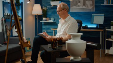 Eski yaratıcı sanatçı, ilham ve yaratıcılık için ders kitabını kullanarak, vazo modeli çizimi için kağıda notlar alıyor. Otantik araçlarla sanatsal tasarım çizmek, başyapıt yaratmak.