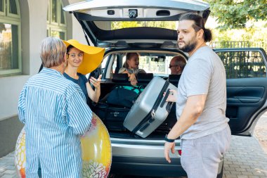Avrupalı bir aile, deniz kıyısındaki tatilde küçük çocuklar, ebeveynler ve büyük ebeveynlerle bırakmak için bagaja bagajlar yüklüyor. İnsanlar bavullarını hazırlıyor ve seyahat çantalarını tatil için hazırlıyorlar..