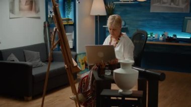 Old woman using laptop to search artistic inspiration on internet, drawing vase model on canvas. Looking at artwork on computer for masterpiece creativity, art and craft sketch.