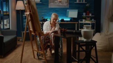 Özürlü bir kadın, sanat aletleri ve ilhamla özgün vazo modelinin taslağını çizmek için kağıda not alıyor. Tekerlekli sandalyede ve çizimde kronik sağlık durumuyla uğraşmak.