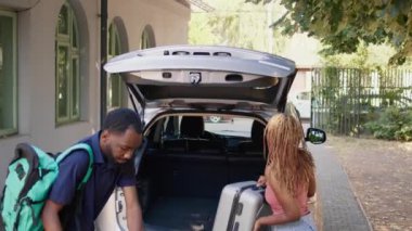 İnsanlar okul gezisi için hazırlanırken bagajlarını ve yük arabalarını arabanın içine koyuyorlar. Afro-Amerikalı çift, tatil için hazırlanırken bagajları yolculuk valizleriyle dolduruyor.