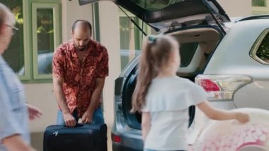 Caucasian family loading voyage luggage inside car trunk while going on summer holiday field trip together. People getting ready for weekend citybreak while putting baggage inside vehicle.
