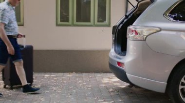 Yaşlı turistler okul gezisi için hazırlanırken bagajları ve yük arabalarını aracın içine koyuyorlar. Emekli çift, yaz tatilinde evlilik yıldönümüne giderken bagaja bagajlarını dolduruyor.