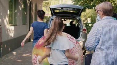 Family loading voyage luggage in car trunk while getting ready for citybreak tour. Grandparents with mother and daughter putting baggage and trolleys inside vehicle while going on holiday journey.
