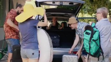 Big family packing voyage luggage in car trunk while getting ready for summer field trip. Happy people loading vehicle with luggage and trolleys while going on weekend citybreak together.