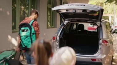 Family loading car trunk with field trip baggage while getting ready for summer holiday citybreak. Caucasian people putting voyage luggage and trolleys in vehicle while going on weekend vacation.