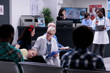 Kadın için steteskop tamamlayan kıdemli tıp doktoru ve özel klinikteki rutin check-up randevusu için hasta kızı. Modern hastane resepsiyonunda bekleyen farklı insanlar var..