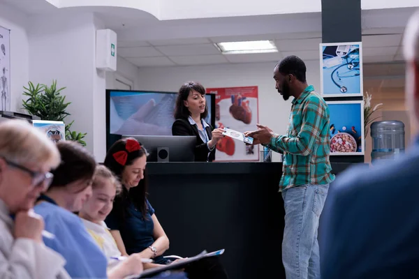 Private Clinic Receptionist Talking African American Patient Offering Him Promotional — Stock Photo, Image