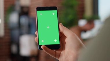 Modern akıllı telefonu elinde yeşil ekran ekranlı serbest çalışan erkek oyuncu boş model şablona bakıyor. Ofisteki cep telefonu arka planında izole edilmiş krom anahtar telif uzayı ile çalışmak.