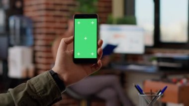 Businessman analyzing smartphone with greenscreen display in startup office. Looking at isolated copyspace template with blank mockup chroma key background, digital mobile phone.