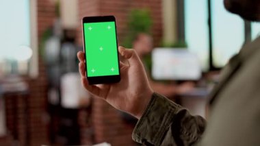 Şirket çalışanı yeşil ekranlı akıllı telefonu tutuyor, izole edilmiş kopyalama alanı ile dijital krom anahtar ekranını kullanıyor. Modern cep telefonunun boş arkaplanı, ofiste uygulama teknolojisi.