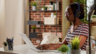 Startup employee listening to music and working from home, using laptop to do remote job on online network connection. Freelancer working on business with computer and headphones.