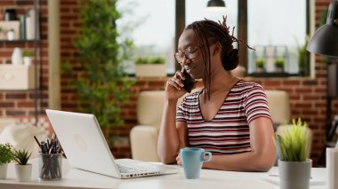 Woman freelancer answering phone call at remote job, working from home and talking to manager on smartphone. Using telephone line to chat remotely, telecommunications network at desk.