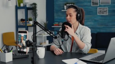 Popular content creator taking a video with smartphone while telling a story. Famous vlogger having professional equipment in living room studio talking with audience about last events.