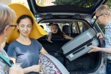 Young child going on vacation with family, preparing to leave on summer holiday at seaside with parents and grandparents. Putting luggage in vehicle trunk to travel to journey destination.