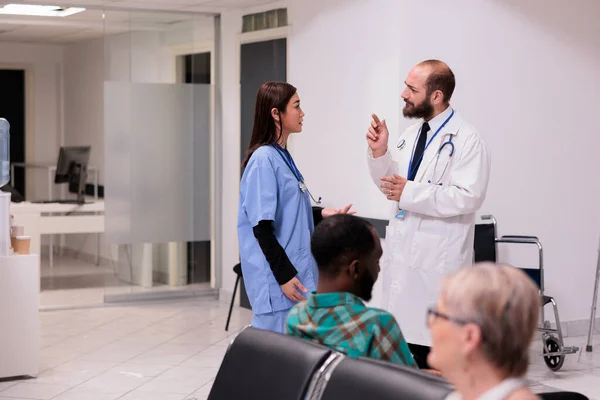 Diverse medical team talking about healthcare support in hospital reception, discussing about patients and appointments at medical facility lobby. Doctor and nurse in waiting room area.