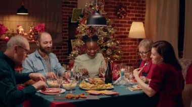 Festive multiethnic family enjoying traditional home cooked food while sitting at Christmas dinner table. Happy people at home celebrating winter holiday together while being positive and peaceful.