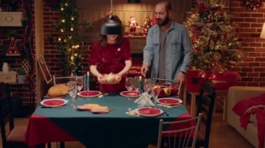 Festive couple welcoming senior guests and young woman at Christmas dinner table. Happy people gathering in living room while celebrating winter holiday together with food and alcoholic drinks.