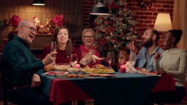 Happy smiling people laughing heartily while talking to camera at Christmas dinner. Joyful family members celebrating winter holiday together while enjoying time together at home. Tripod shot