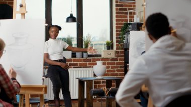 Eğitim atölyesinde çizim pratiği öğretmek için masadaki vazo modelini gösteren genç sanatçı. Kişisel beceriler geliştirmek ve tuvale çizim yapmak için sanatsal sınıf programı.