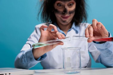 Close up of mad foolish scientist testing experimental serum by adding unknown substance while on laboratory space. Crazy chemist with messy hair and dirty face mixing unstable chemical compounds.