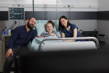 Mother and father resting with sick little girl while enjoying family tv series. Caring parents sitting beside hospitalized daughter while watching television show inside children healthcare facility.