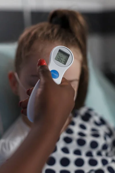 Close up shot of african american nurse measuring sick little girl body temperature using thermometer. Children healthcare facility medical staff examining disease evolution of ill kid under treatment