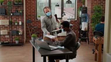 Yüzü maskeli iş adamları başlangıç projesinde takım çalışması yapıyorlar. Şirket sunumunu planlamak için veri tabloları ve istatistiklerle çalışıyorlar. Salgın sırasında ofis işindeki çeşitli insanlar.