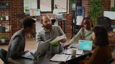 Diverse team of coworkers analyzing business charts on documents, working on presentation report in boardroom. Using data on documents to plan research in corporate management meeting.