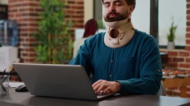 Office employee with neck collar brace working after accident injury, being in pain at job. Injured man feeling hurt and wearing cervical foam to cure physical ache and tension, business office.