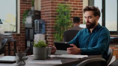 Dijital tablet üzerinde çalışan işadamı, yönetim sunumuna veri eklemek için çevrimiçi bilgi ve araştırma kullanarak başlangıç ofisinde e-posta gönderiyor. Rapor oluşturmak için beyin fırtınası fikirleri.