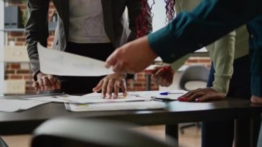 Diverse team of coworkers looking at business charts on documents, analyzing research information and statistics on diagrams review. People using papers with infographics data report. Close up.