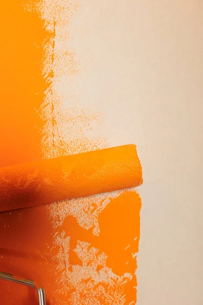 Rolling brush with orange paint to renovate and redecorate apartment walls, changing surface color with dye. Using round paintbrush with bristles and container with liquid to repaint. Close up.