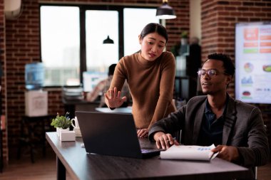 Multiethnic team of partners working on laptop in disability friendly office, man with physical health condition at work. Company worker with impairment brainstorming ideas with woman.