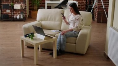 Excited woman reading work email about job promotion while working remotely from home. Cheerful young adult person getting notified on mobile about salary raise while sitting on sofa.