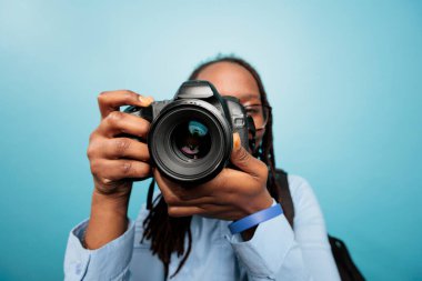 Amateur photographer taking photos with modern DSLR device while standing on blue background. Photography entusiast enjoying taking pictures with photo camera. Studio shot