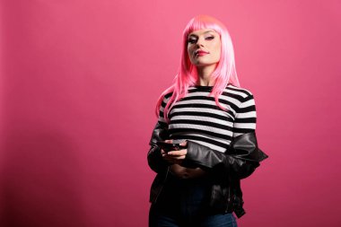 Attractive female model with smartphone and leather jacket sitting over studio background, feeling confident and funky with trendy rocker style. Wearing sensual sexy and punk fashion items.