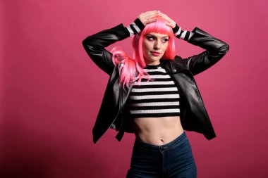 Young stylish woman with pink hair wearing punk leather jacket to be trendy and advertise rocker fashion style. Female model feeling funky and attractive, standing over studio background.