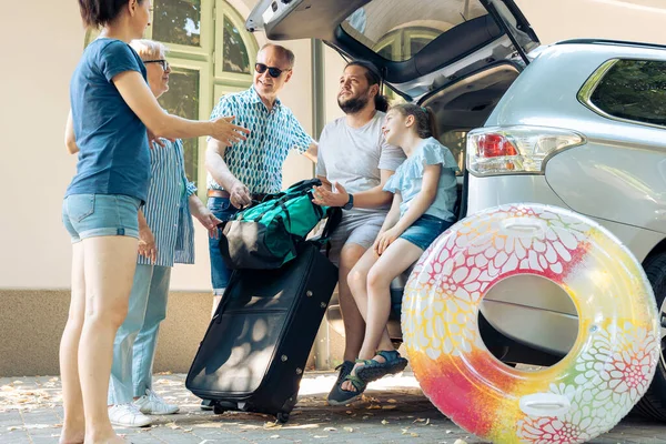 European family loading bags in trunk vehicle, preparing to leave on seaside vacation journey. Little child with parents and grandparents travelling with automobile to go on summer holiday.
