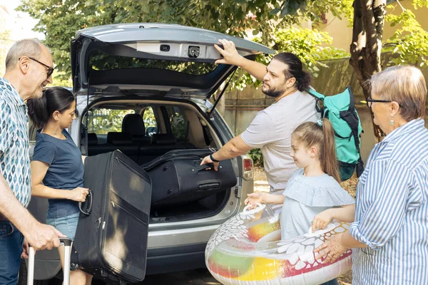 Big european family going on holiday vacation and loading baggage in automobile trunk. Child travelling with parents and grandparents at seaside during summer, putting luggage in vehicle.