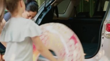 People putting baggage and trolleys inside car while getting ready for vacation citybreak. Positive mother and daughter loading voyage luggage in vehicle trunk while going on summer holiday.
